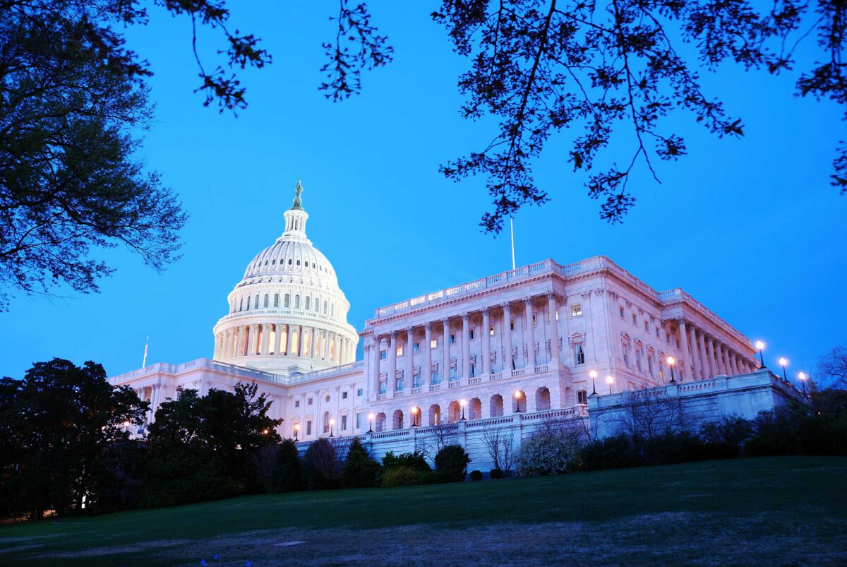 The US Capitol building seen from behind some trees on a blue sky